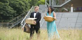 Ein festlich gekleideter Besucher und eine Besucherin tragen Ihr Picknick im Garten